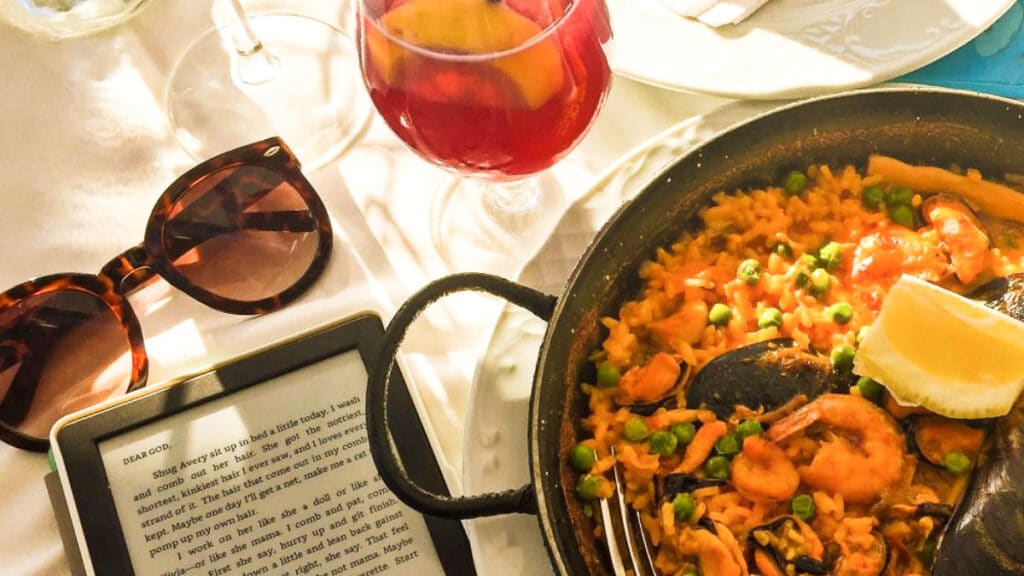 A serving of paella with kindle, sunglass, and a glass of drink on the side