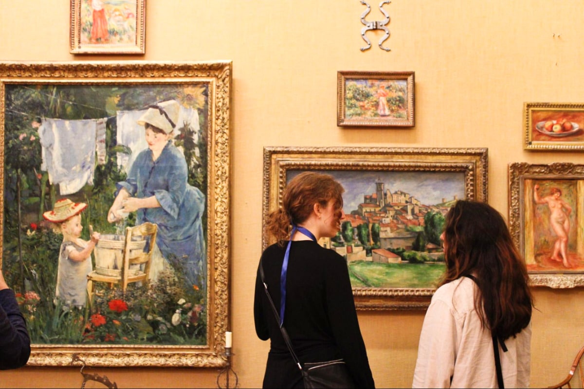 Two people in front of the framed paintings