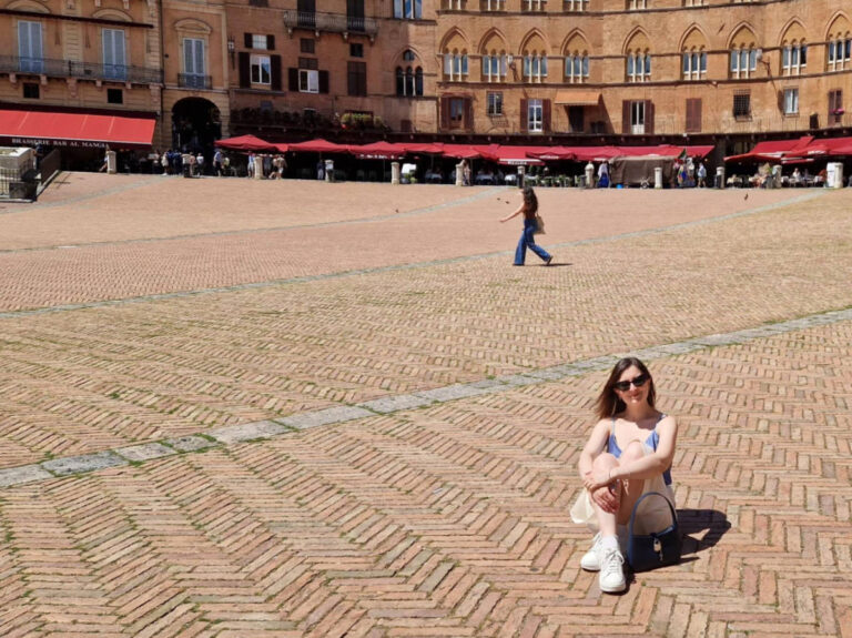 The author Giorgia Giustolisi, sitting on the red brick floor of Piazza del Campo