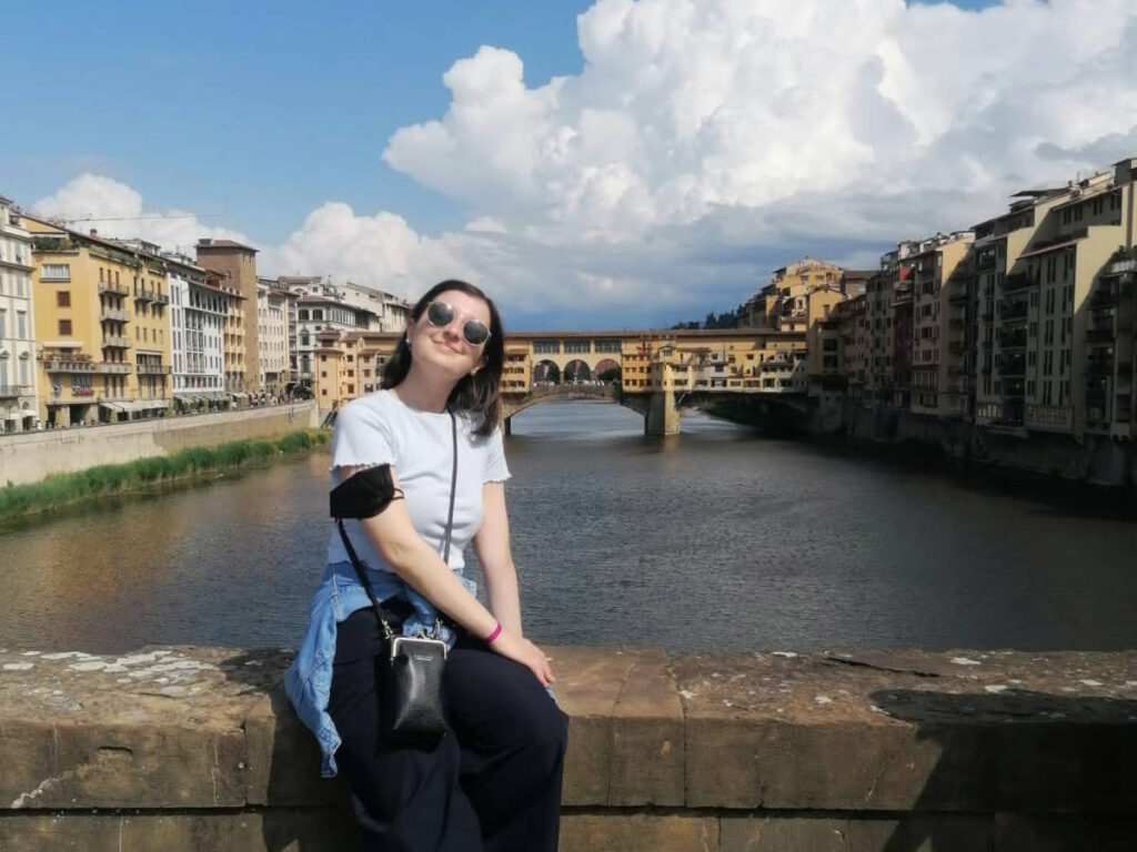 The author Giorgia Giustolisi, posing for a photo at the Ponte Santa Trinità with the Ponte Vecchio in the background