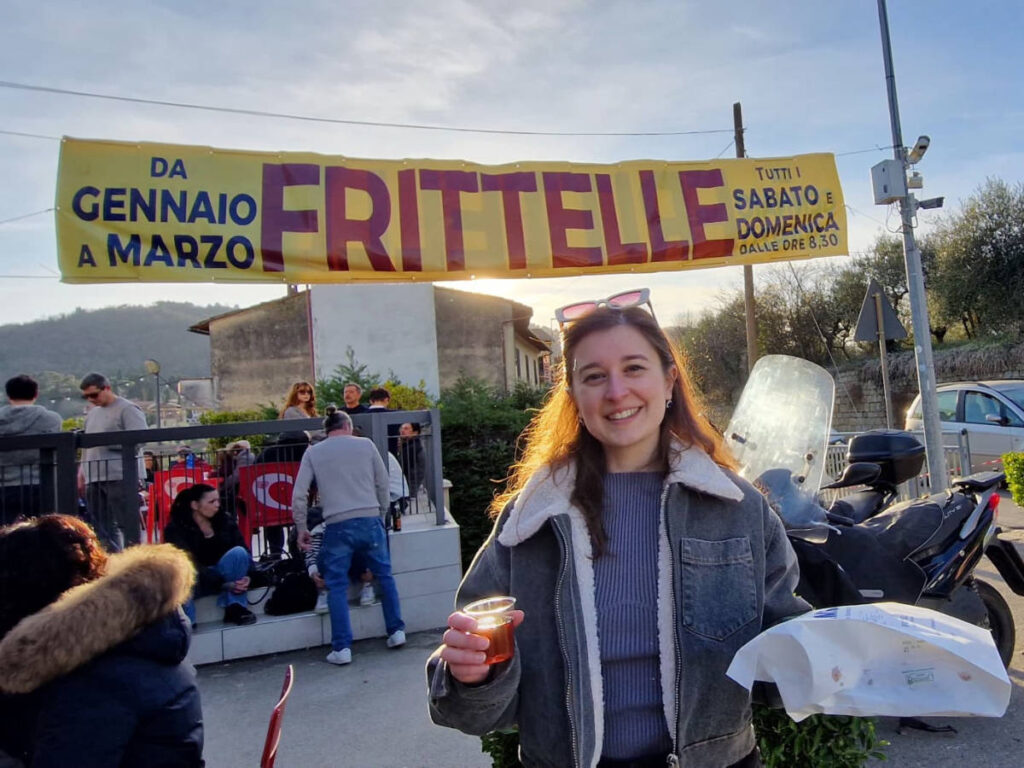 The author Giorgia Giustolisi, holding a pack of frittelle and drink in San Donato