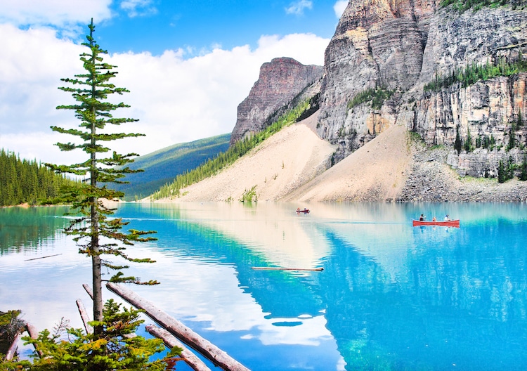 A red canoe floats in a glacial blue lake among mountains in British Columbia