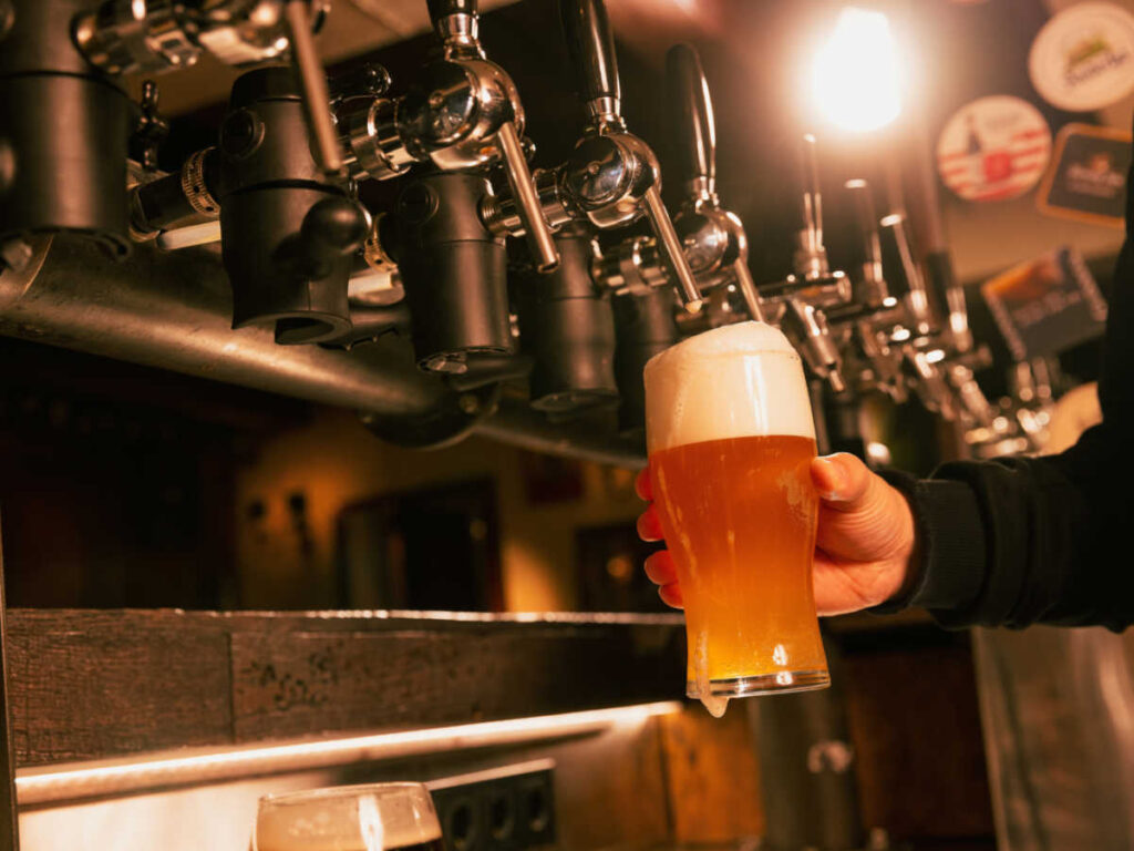 A hand pouring cold foamy beer from tap into glass
