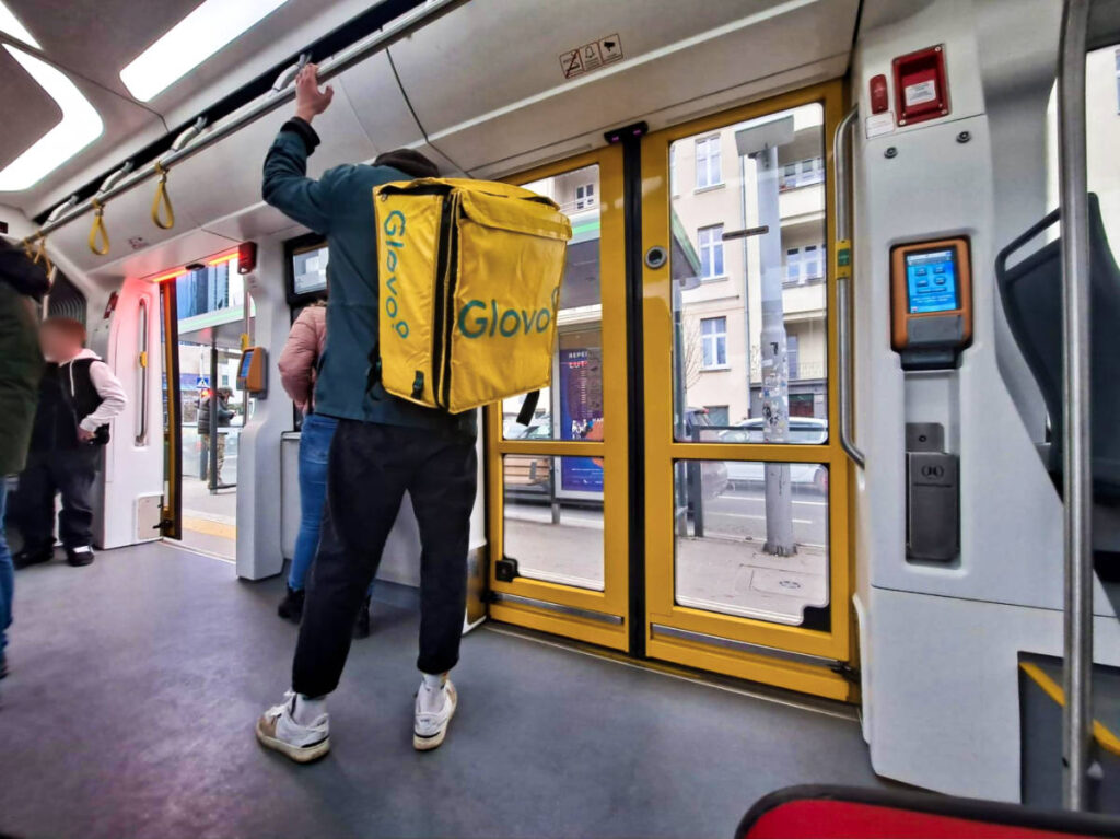 A man wearing a Glovo delivery backpack while riding on a train