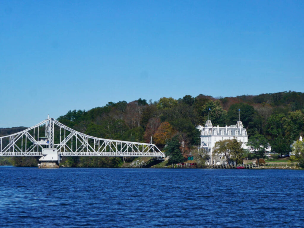 View of the bridge and the Goodspeed Opera House surrounded by greenery seen from across the water