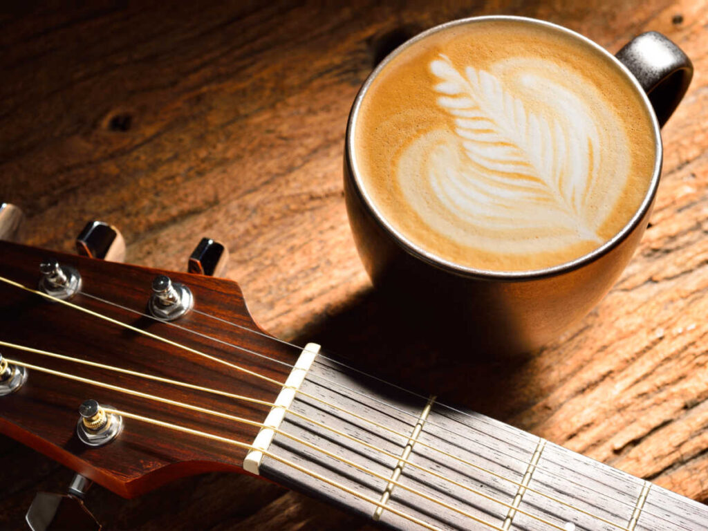 A cup of coffee beside a guitar on a wooden table
