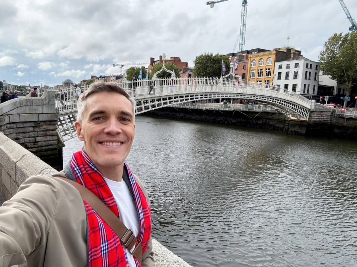 Nate Hake smiling for a photo with the Ha’Penny footbridge on the background