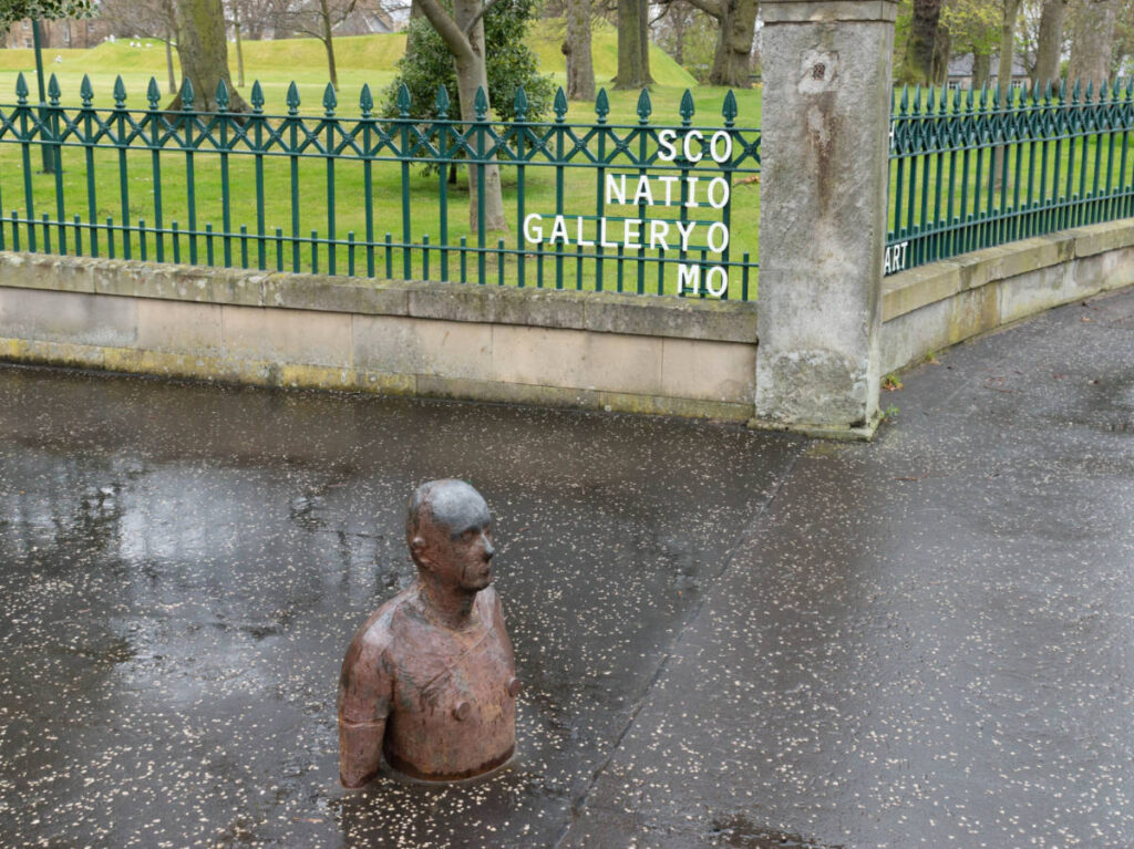 A statue half buried on the ground outside the Scottish National Gallery of Modern Art
