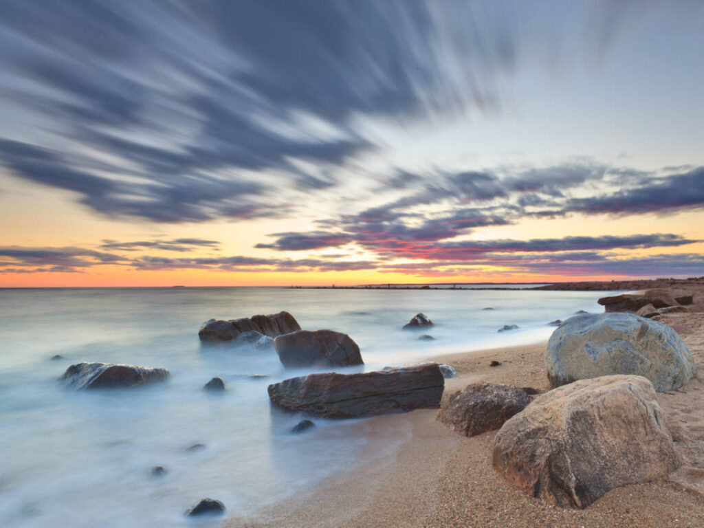 Scenic view of the sunset from the white sand with huge rocks on the shoreline of Hammonasset Beach State Park