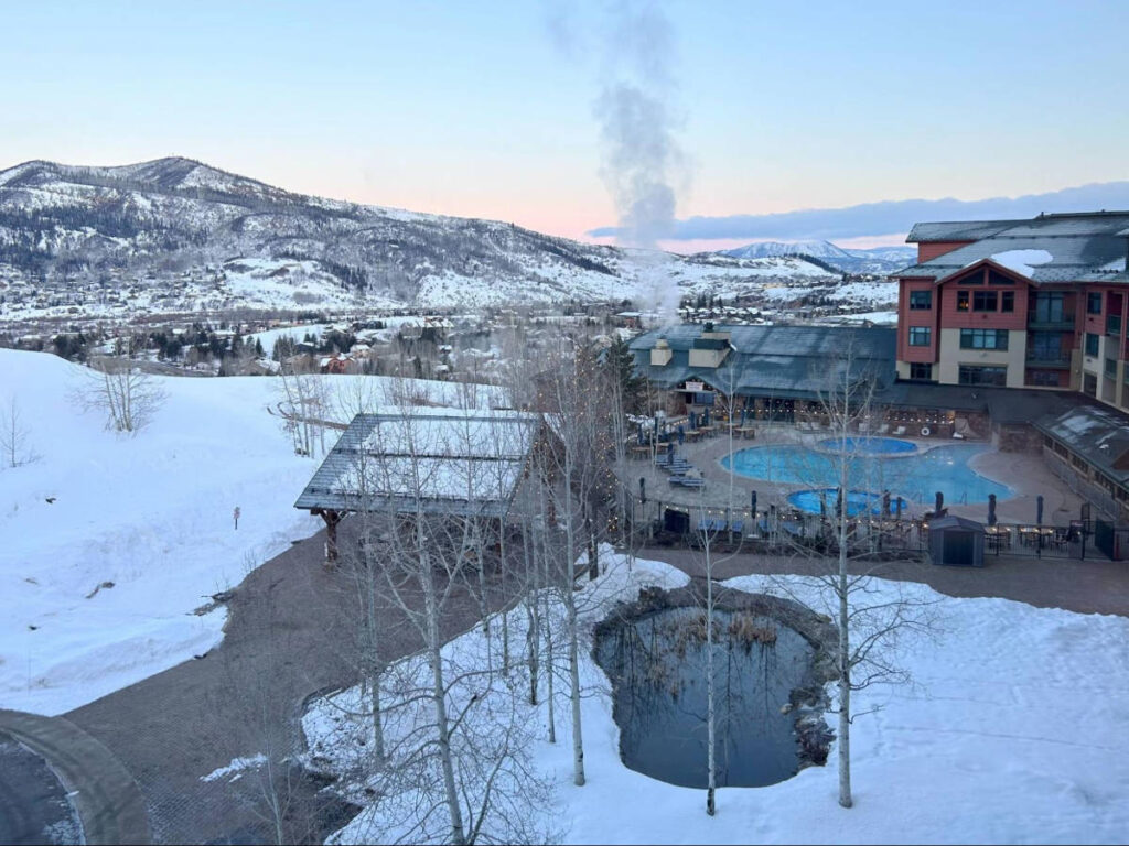 overlooking view of the heated pool and hot tub with scenic views covered in snow