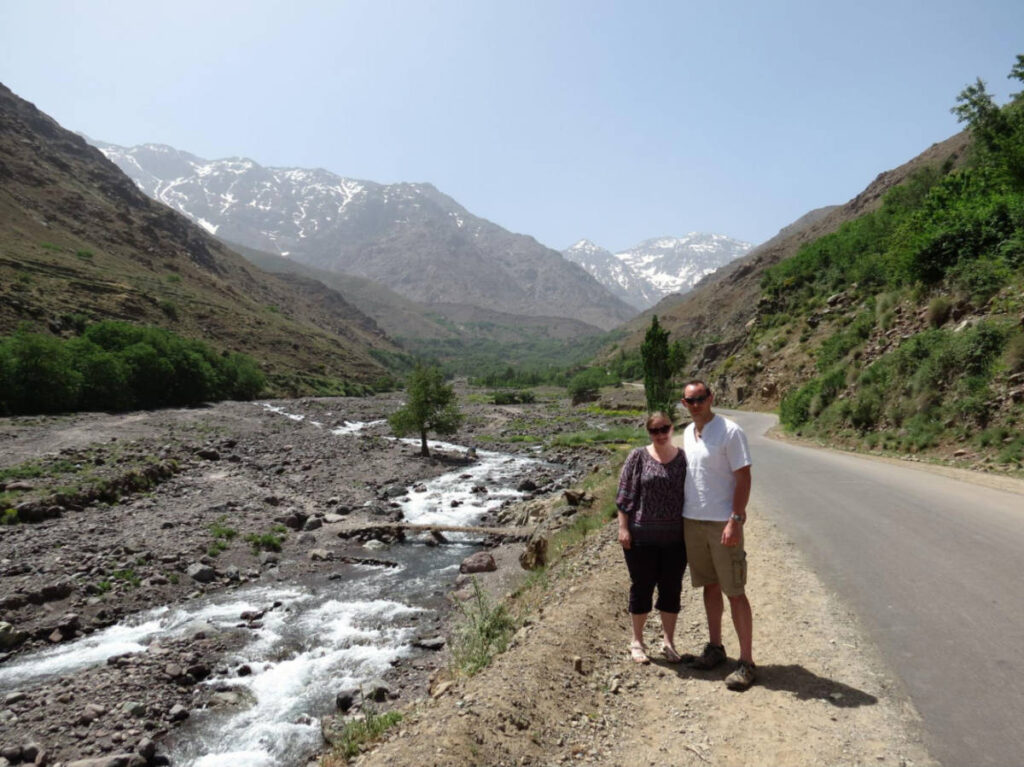 The author Heather Cole and her husband, smiling for a photo with the views of the High Atlas Mountains