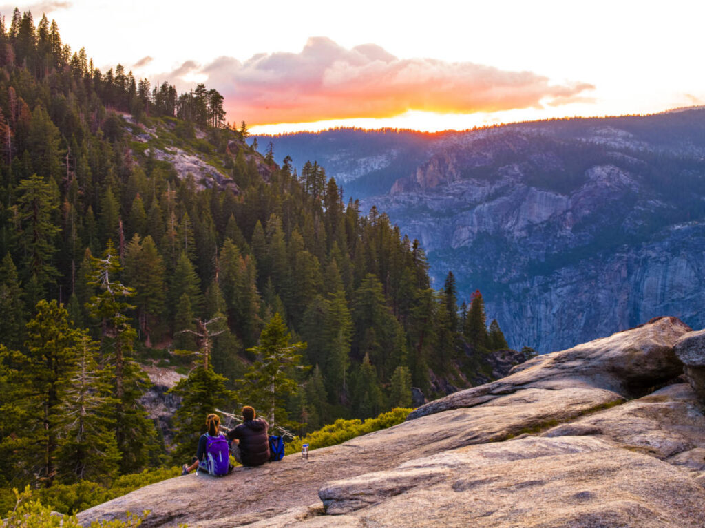 Two hikers sitting on the ground while enjoying the sunset view at Yosemite National Park