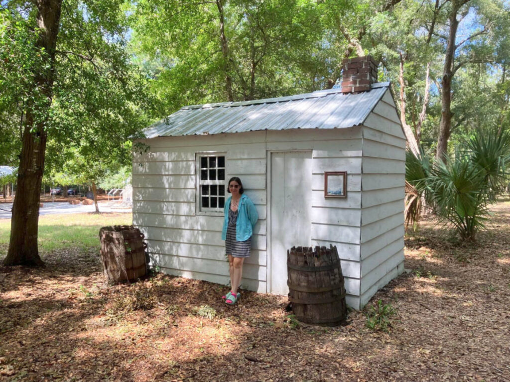 The author Meg standing in front of a small white house at Historic Mitchelville Freedom Park
