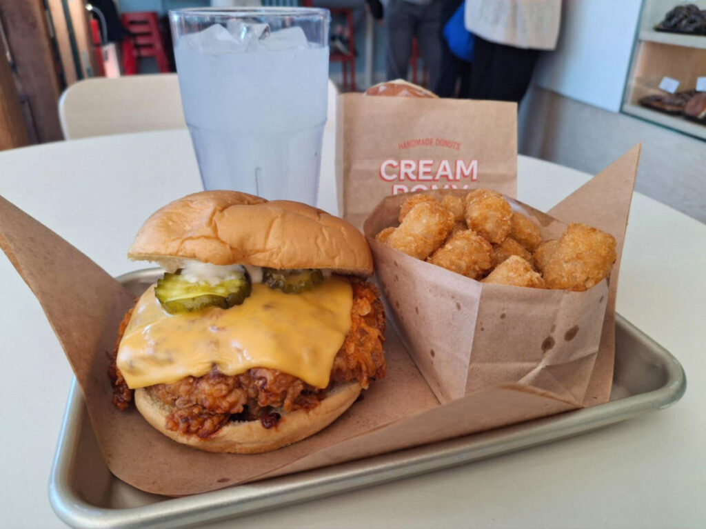 A tray with “Hot Nash” chicken sandwich and a glaze donut on a bag at Cream Pony