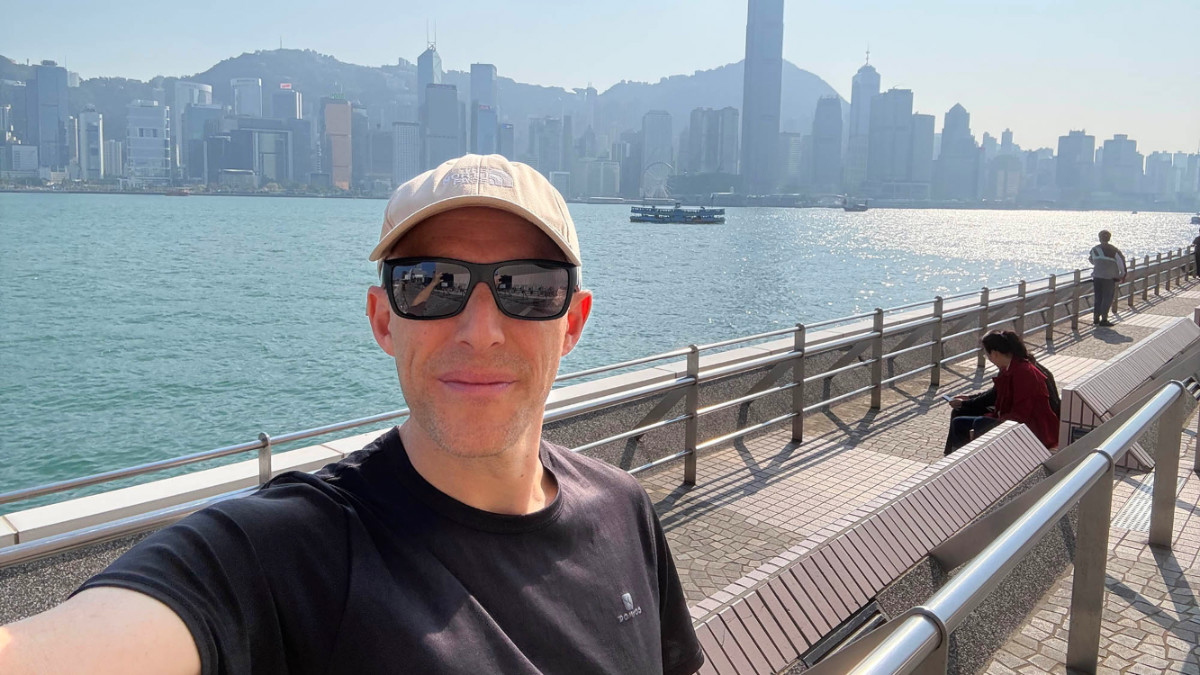 The author Ian Trower, smiling for a photo with the view of Tsim Sha Tsui Promenade