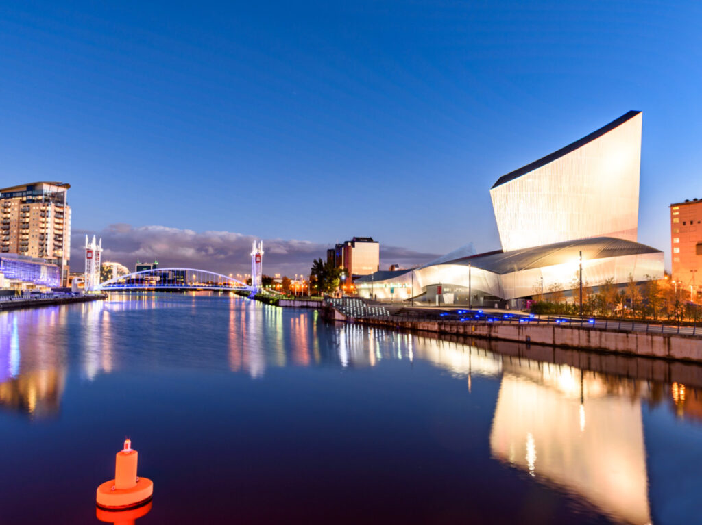 View of the illuminated cityscape reflecting on the water in the quayside Imperial War Museum North at night