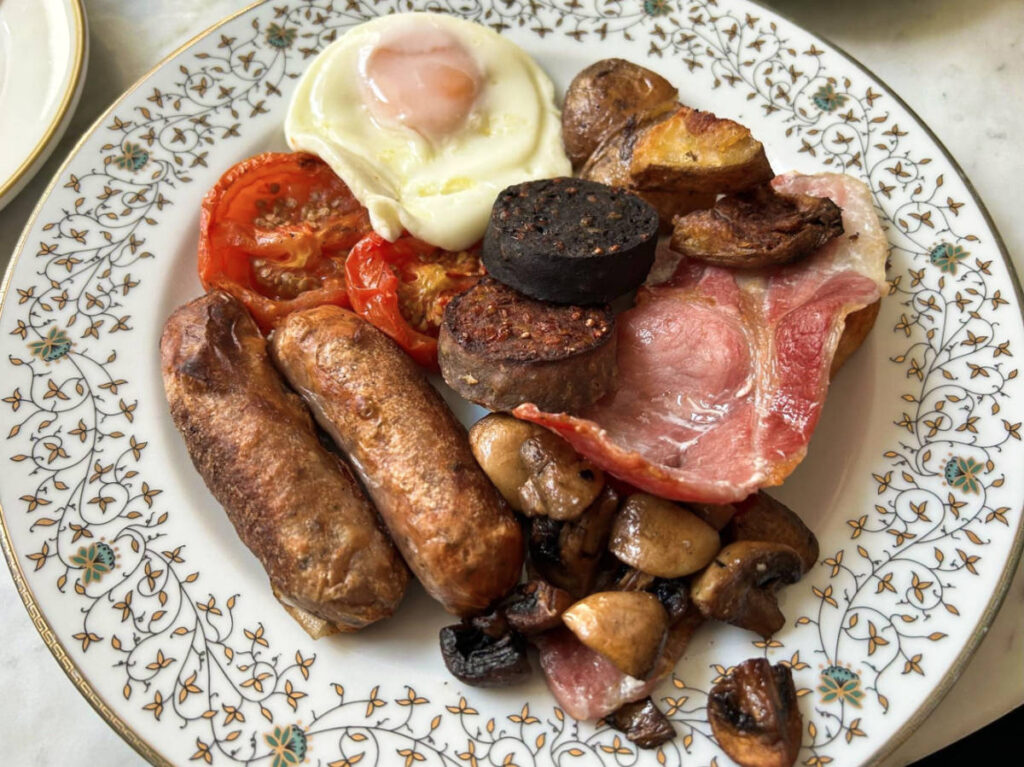 A plate of Irish breakfast with bacon, sausages, eggs, mushrooms, grilled tomatoes, and potatoes