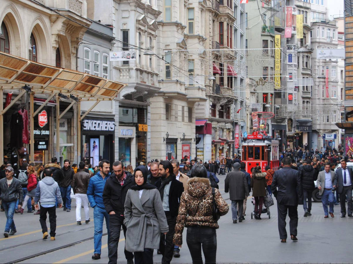 A city street with people walking and shopping, as the historic tram moves along Istiklal Caddesi