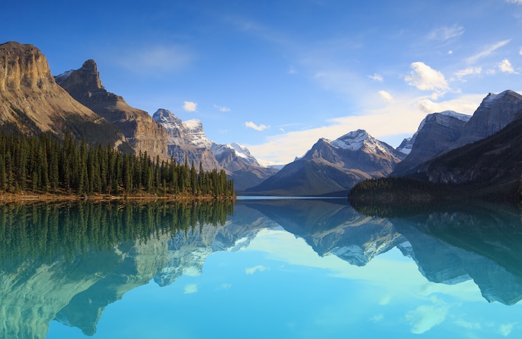 A glacial turquoise lake reflects the trees and mountains of Jasper National Park Alberta