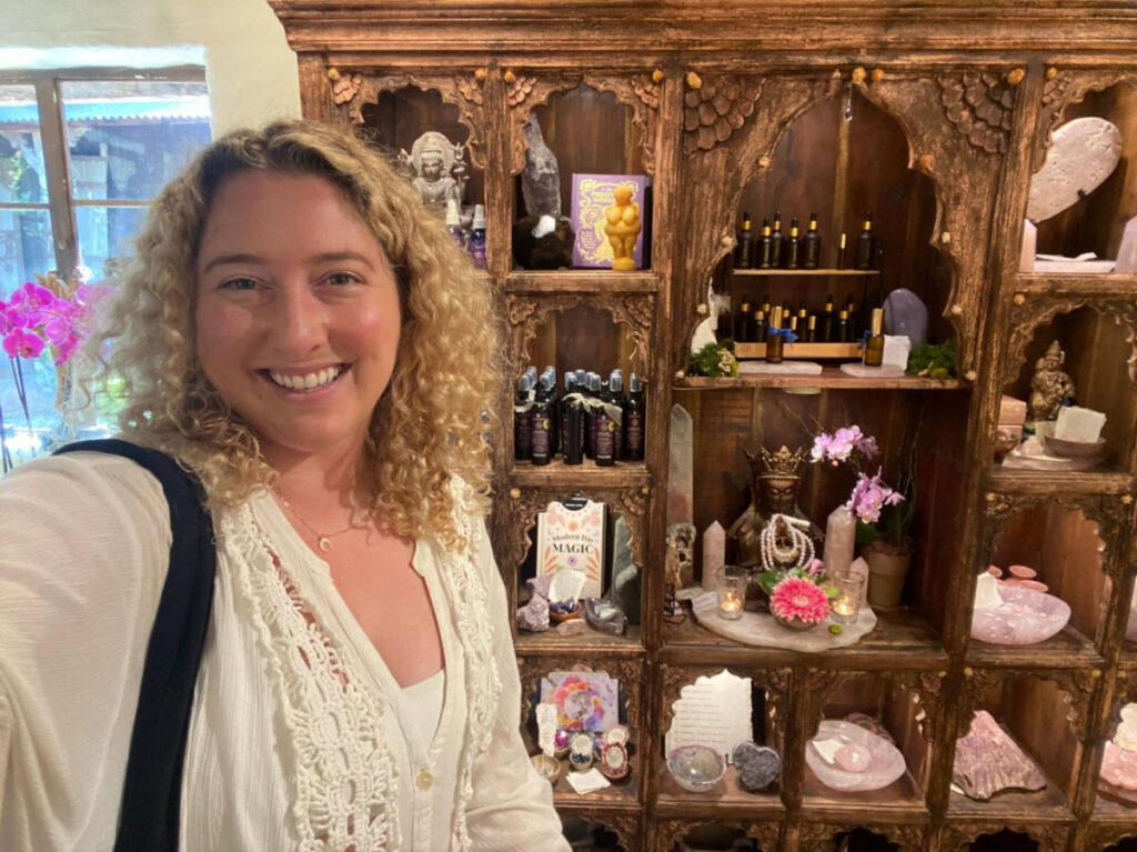 The author Jess Levy, smiling in front of a display case inside The Sacred Space