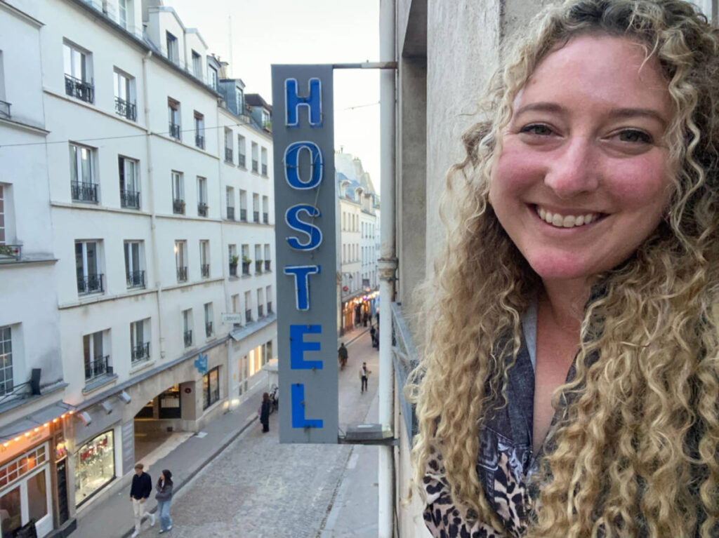 The author Jess Levy smiling for a photo with the hostel signage