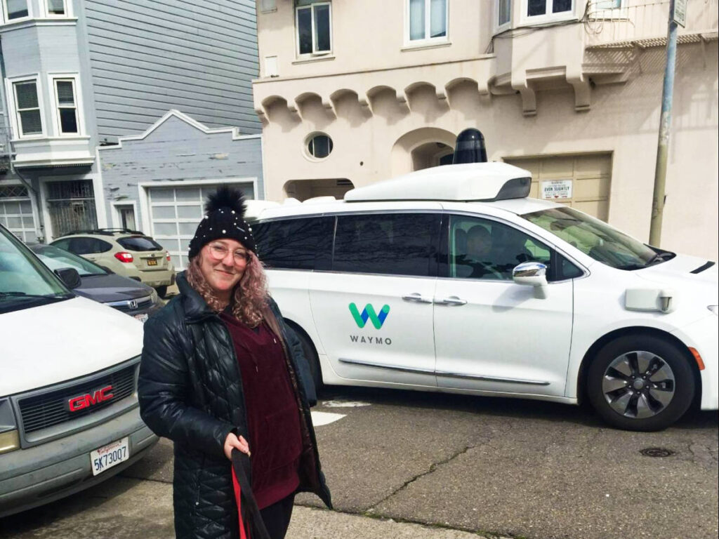 The author Jess Levy, posing with the Waymo self-driving car in the background