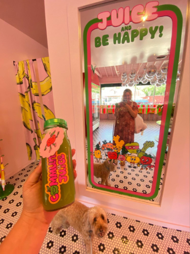 The author Jess Levy and her pup, smiling in front of a mirror inside the colorful interior of Community Juice