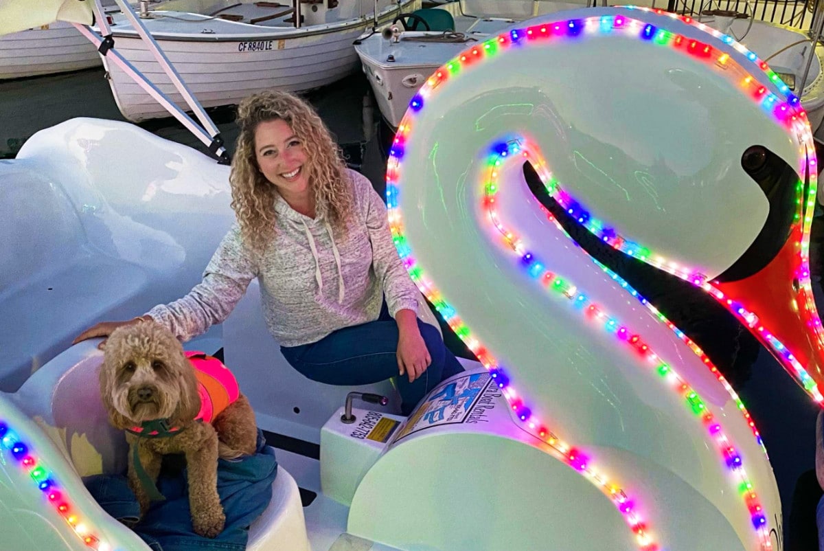 Travel Lemming Writer, Jess and her puppy riding on neon-lit swan boat