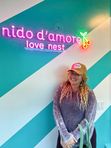 The author Jess Levy posing for a photo at the signage of nido d’amore lounge