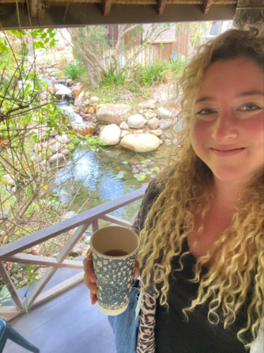 The author Jess holding a drink at the pagoda with a view of the stream