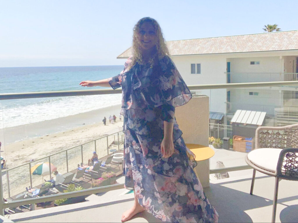 The author Jess Levy, standing at the balcony with ocean view in the background in Beach Terrace Inn