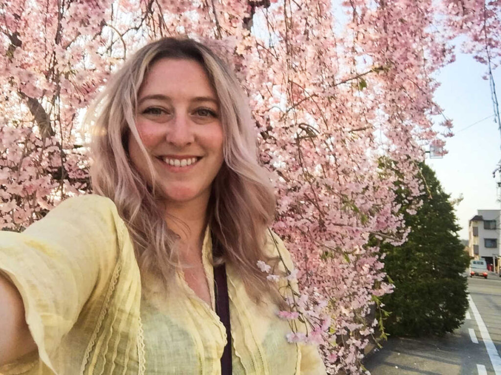 The author Jess Levy, smiling for a photo with the cherry blossoms in the background