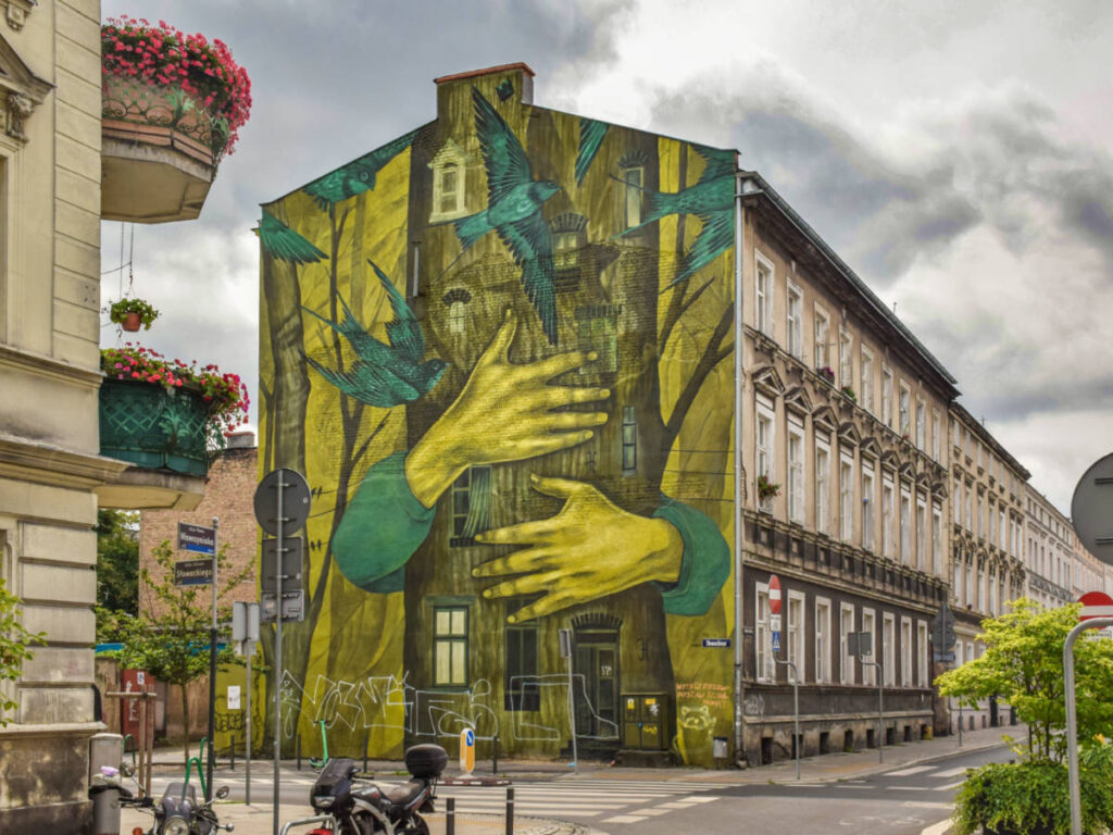 A mural of a hand hugging the tower with birds around, painted on a building wall.