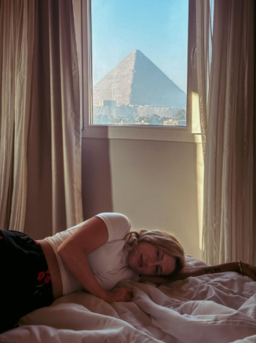 The author Kate McMahon, lying on the bed with the view of the pyramid from the rented apartment