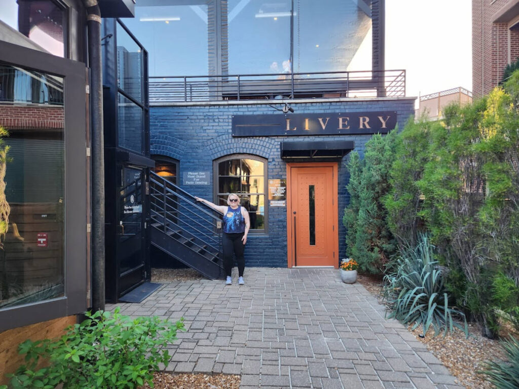 The author Kelsey Nighthawk posing for a photo at the entrance of Livery
