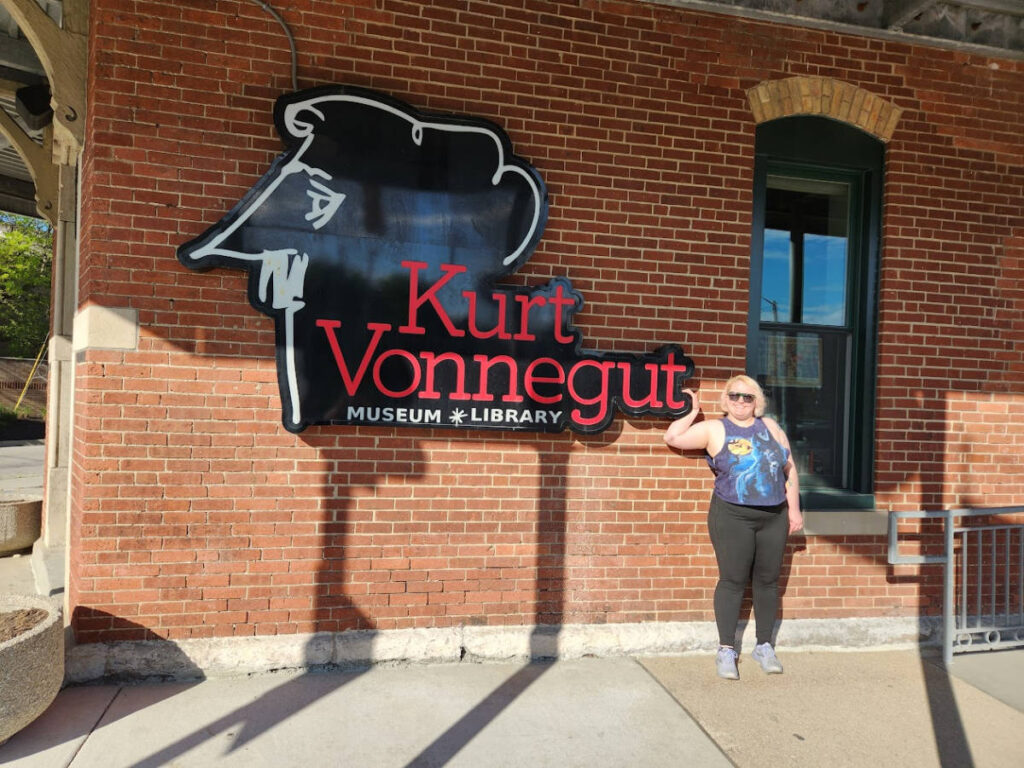 The author Kelsey Nighthawk posing near the sign of The Kurt Vonnegut Museum