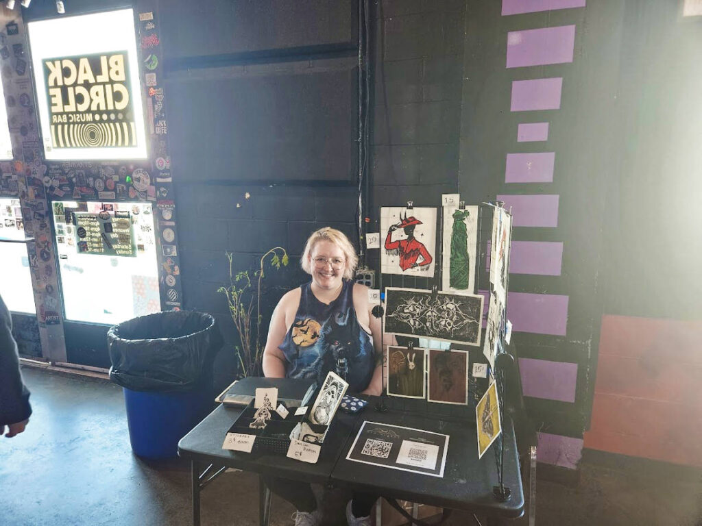 The author Kelsey Nighthawk sitting in one of the art booth at the Black Circle