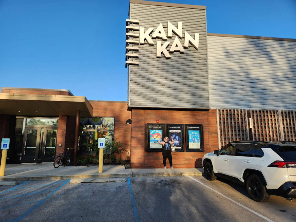 The author Kelsey Nighthawk posing and pointing the signage of Kan-Kan Cinema and Restaurant
