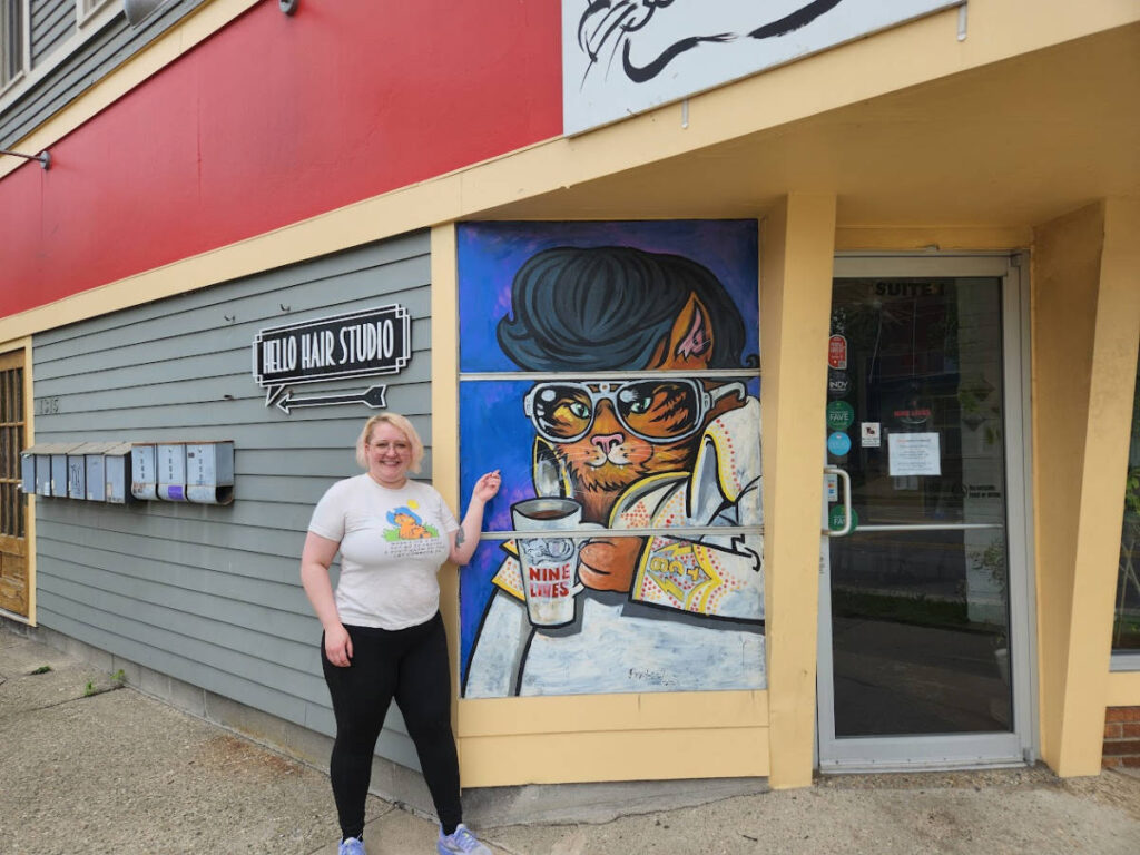 The author Kelsey Nighthawk pointing the Elvis Cat Mural at the Nine Lives Cat Café