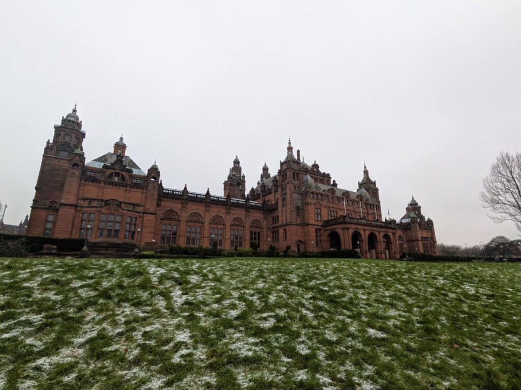 View of Kelvingrove Art Gallery and Museum under an overcast sky and framed by a lightly snow-dusted lawn 