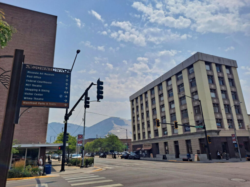 A sign showing the way to local landmarks in Missoula, with “The M” store at the background