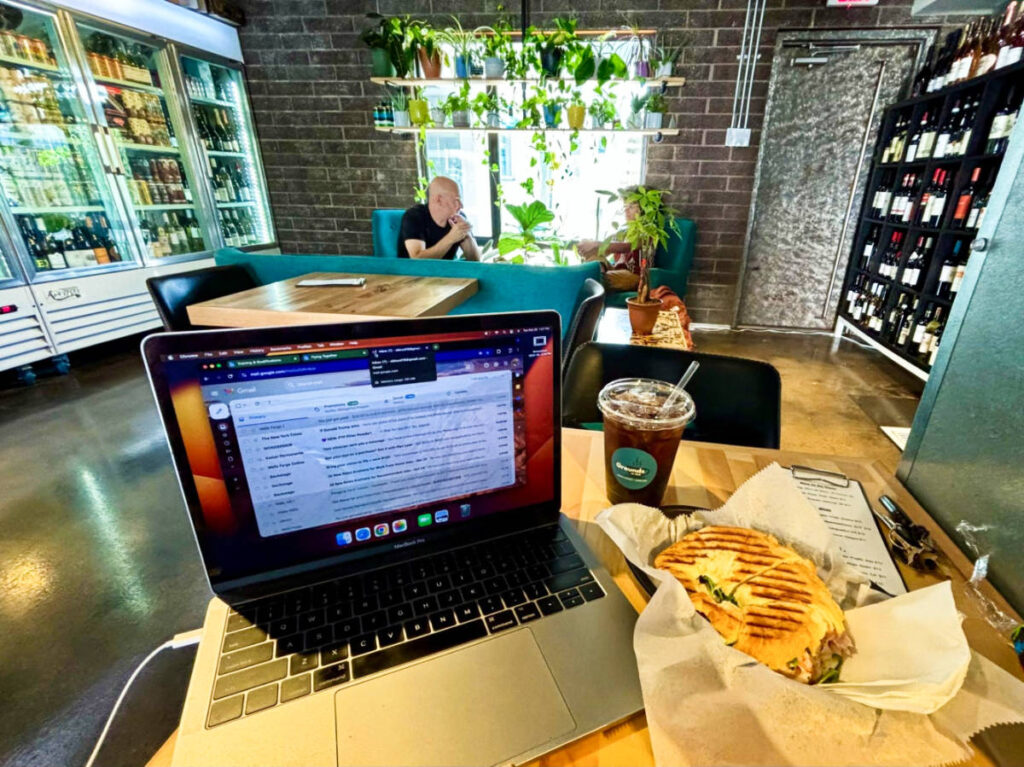 A laptop with turkey pesto panini on a table inside the Grounds on 2nd coffee shop