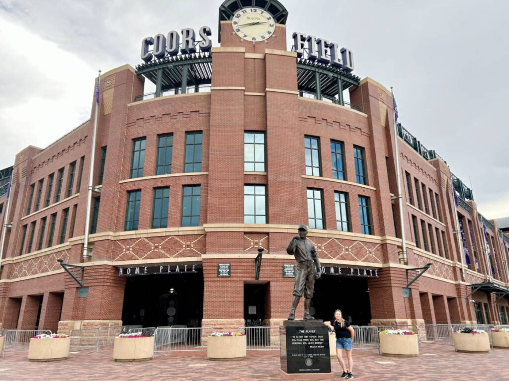 The author, Laura Falin posing for a photo with a statue outside Coors Field
