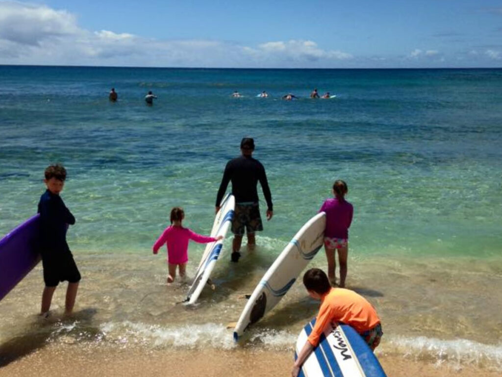 A family walking to the ocean while holding their paddleboards