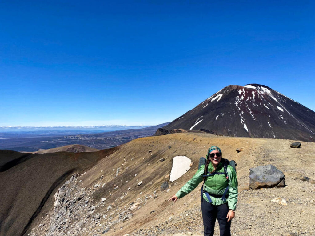 The author Laura McFarland standing right next to Mt. Ngauruhoe against a clear blue sky