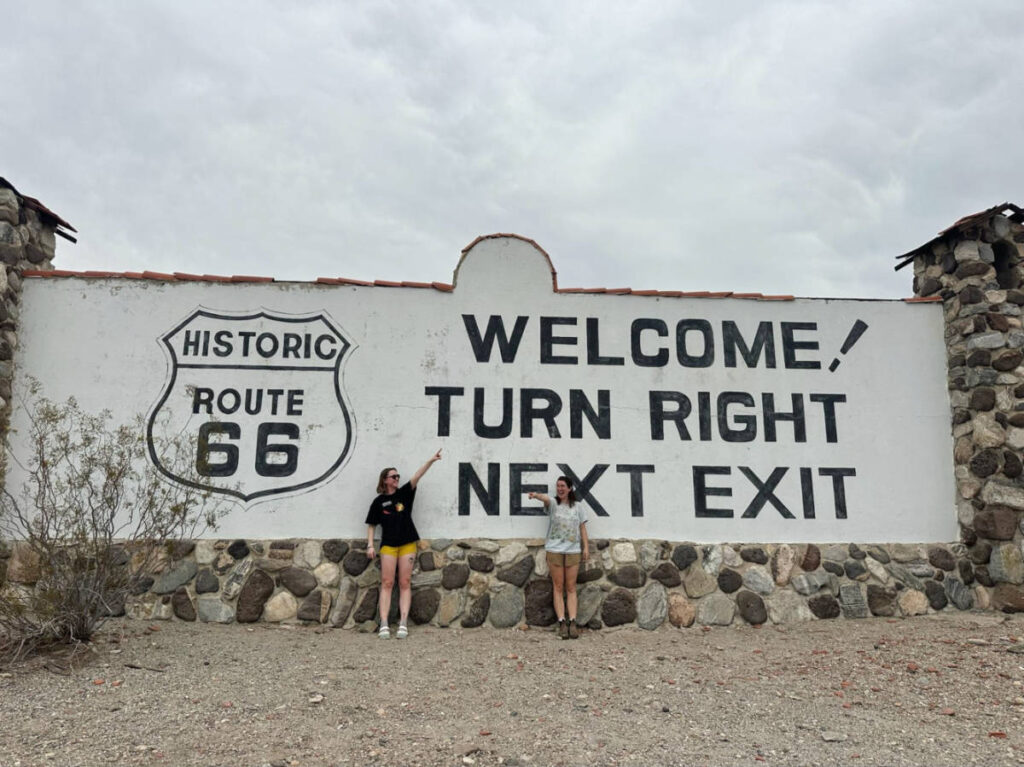 The author Laura McFarland and her partner, posing for a photo in front of the Route 66 sign outside of Needles