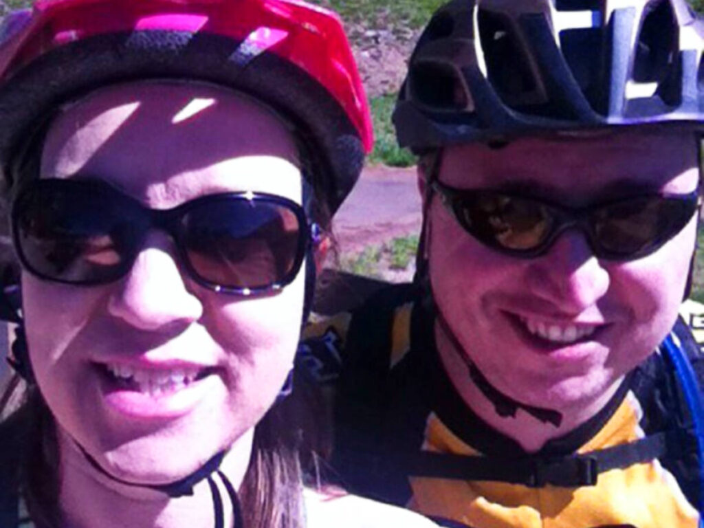 The author Laura Falin and her husband smiling for a photo while wearing their cycling helmets