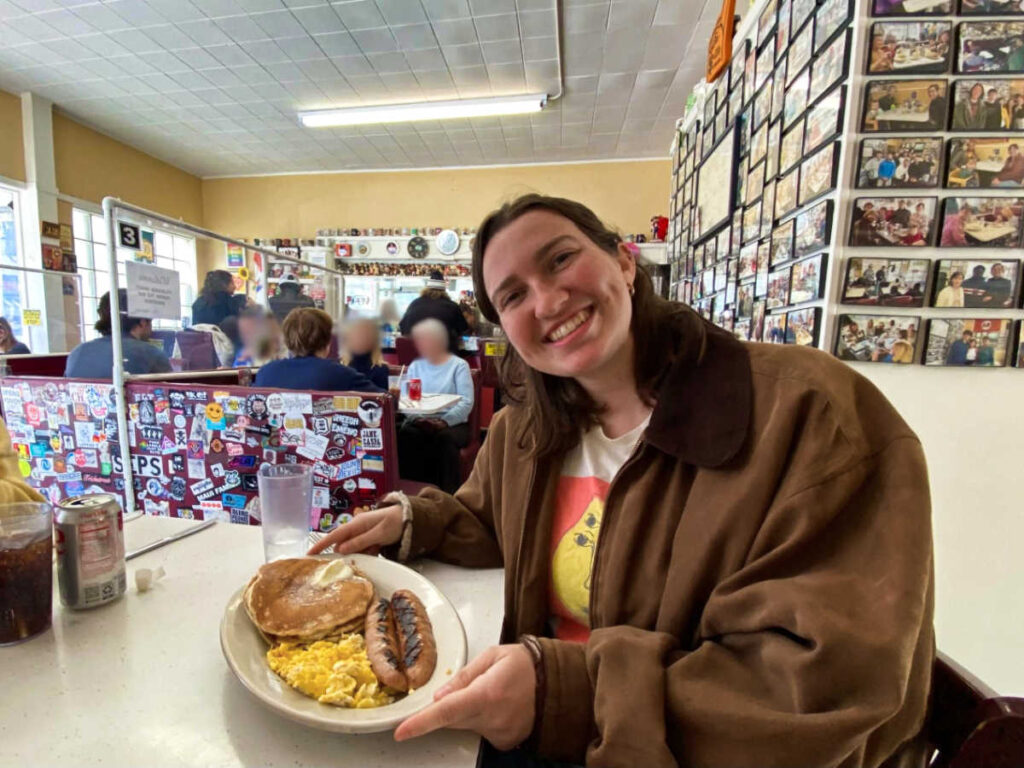 The author Laura holding a plate with pancakes, sausages and scrambled eggs