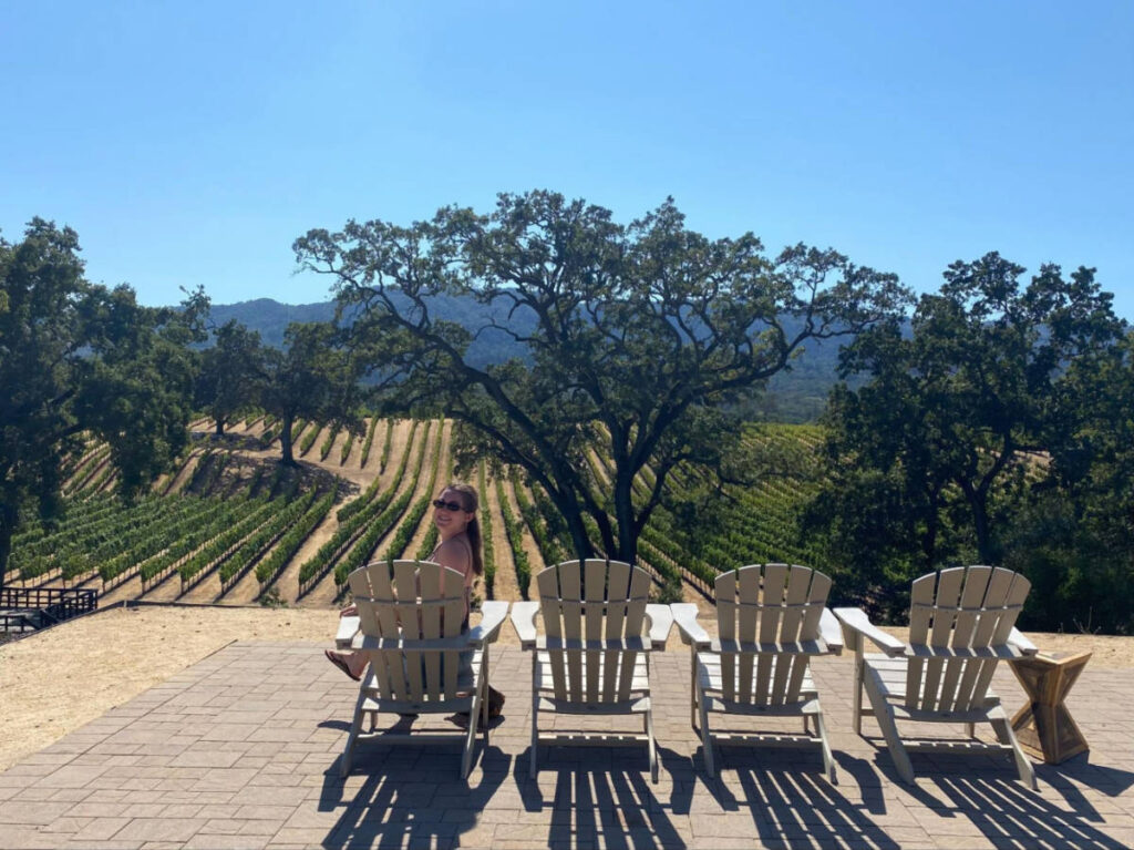 The author Laura McFarland, sitting on a chair overlooking the vineyard at a winery in Sonoma