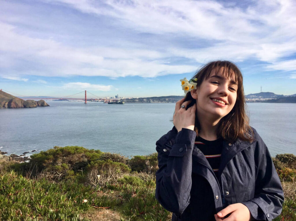 The author Laura McFarland's friend, posing for a photo with flowers on her ear with the Golden Gate Bridge in the background
